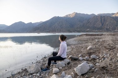 Kadın, doğanın tadını çıkarırken bir gölün kıyısında meditasyon yapıyor. Macera, doğa ve seyahat kavramı.