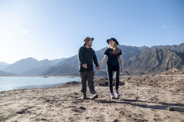 Dağların ve gölün doğal manzarasıyla dışarıda yürürken el ele tutuşan çift. Doğa ve seyahat kavramı.