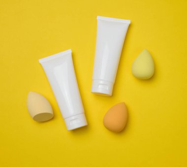 Krem, jel ve diğer kozmetik ürünleri için beyaz plastik tüpler ve sarı arka planda süngerler.