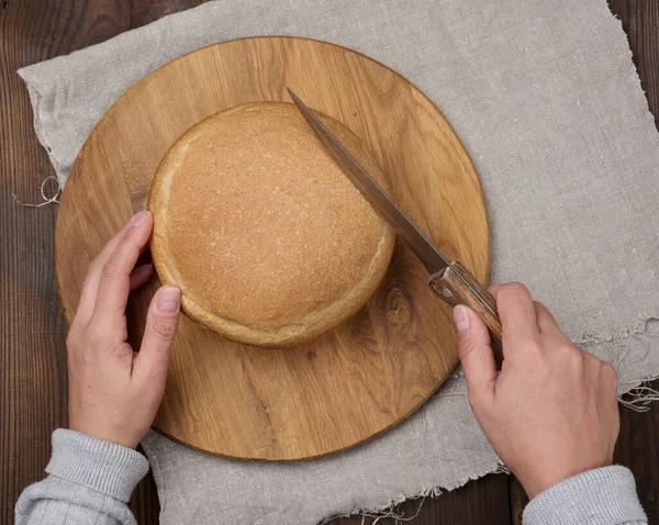 stock image Round baked bread on a wooden board, brown table. View from above