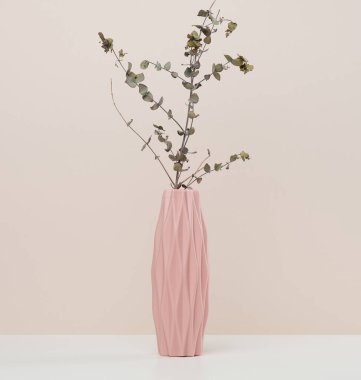 Beyaz masa üzerinde okaliptüs dalı olan pembe seramik vazo