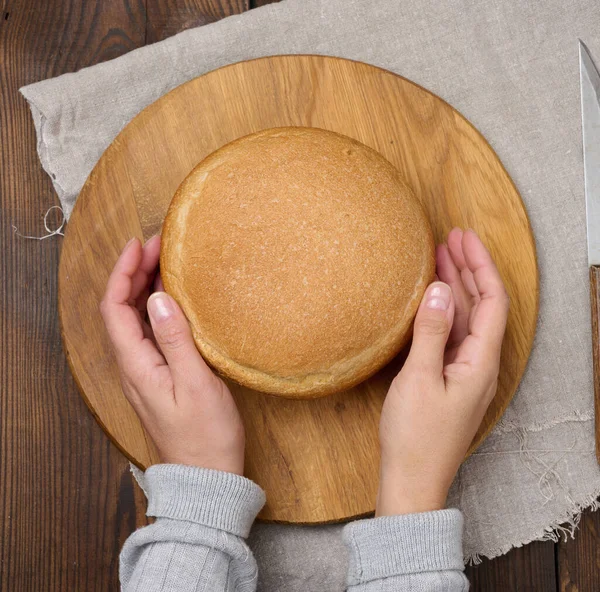 stock image Round baked bread on a wooden board, brown table. View from above