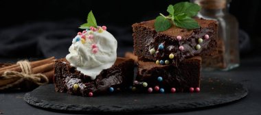 Bir kepçe dondurmanın üstünde, siyah bir masanın üzerinde çikolatalı kek parçaları.