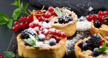 Fruit tart with red currants sprinkled with powdered sugar on a black table