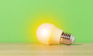 A glass white lamp shines with yellow light on a green background. New idea