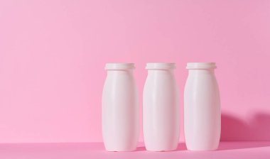 White plastic bottles for yogurt and dairy products on a pink background