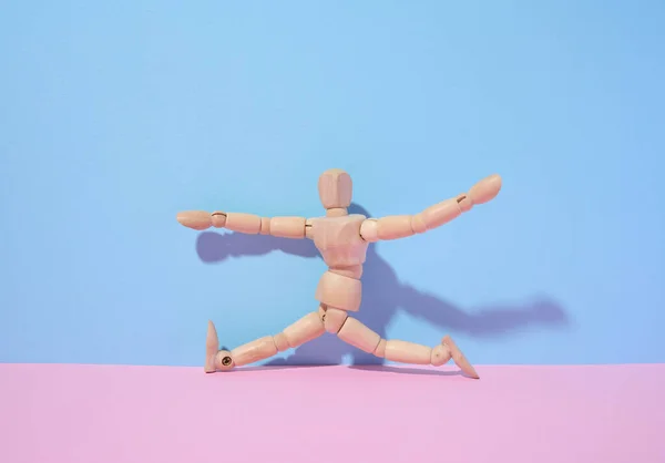 Wooden puppet man on a blue background, a pose in a twine. Sports