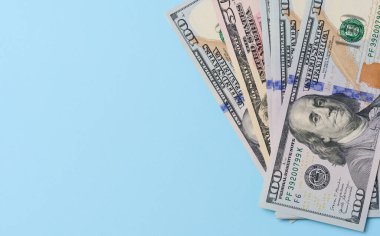 One hundred dollar bills with a portrait of Benjamin Franklin on a blue background, top view