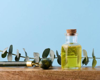 Sarı yağı ve okaliptüs dalı olan şeffaf cam şişe, kozmetik ürün.