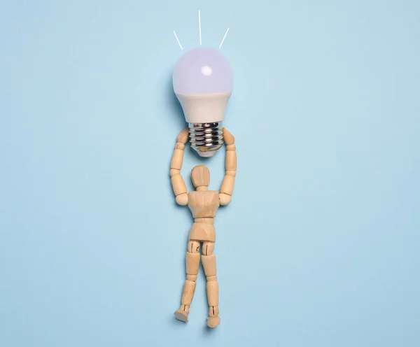A wooden mannequin holds a glass lamp against a blue background, representing the concept of searching for new ideas and optimal solutions
