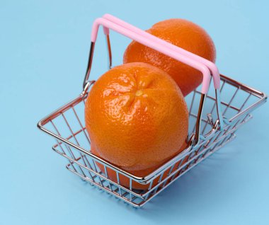 Ripe mandarins in a miniature metal shopping cart on a blue background, citrus price increase concept
