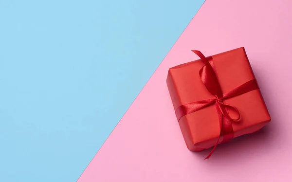 Square box tied with a red bow on a blue-pink background, top view