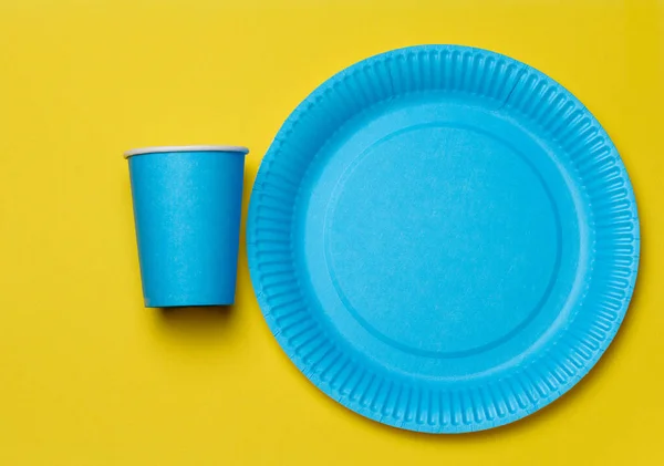 Round disposable blue paper plates and cups for a picnic, recyclable waste, top view.