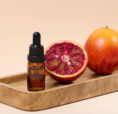 Kahverengi cam bir pipetle bej arka planda kırmızı bir portakal, yağlar ve kozmetik ürünler.