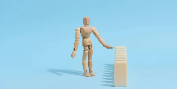 Wooden toy mannequin keeps dominoes from falling, risk prevention concept