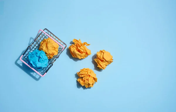 Crumpled balls of paper in a miniature shopping cart on a blue background. New ideas and innovations