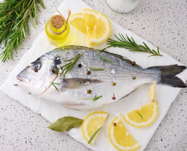 Beyaz tahtada çiğ dorado balığı ve yemek pişirmek için baharatlar, beyaz masada üst manzara.
