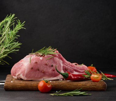 Kemikte çiğ domuz filetosu ve siyah arka planda tahta kesme tahtasındaki baharatlar. Öğlen ve akşam yemeği için porsiyon