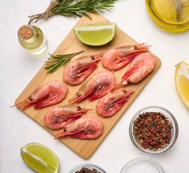 Tahtada kaynamış karides, limon ve limon dilimleri, beyaz arka planda baharatlar, üst manzara.