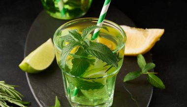 Limon, limon, biberiye filizi ve nane yapraklı şeffaf bardakta limonata.