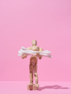 Ahşap manken pembe arka planda bir yığın kulak çubuğu tutuyor.