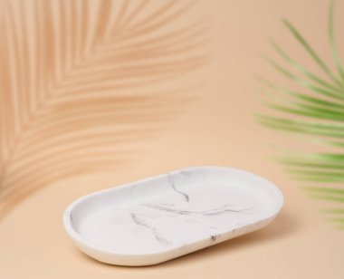 Bej bir zemin üzerinde boş oval beyaz mermer standı ve palmiye yapraklarından bir gölge, kozmetik ürünleri ve ürünleri sergilenecek bir yer