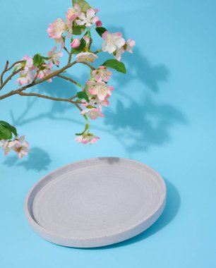 Mavi arka planda yuvarlak boş bir tabak ve çiçekli bir kiraz dalı, kozmetik ürünleri ve ürünleri sergilenecek bir yer