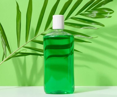 Yeşil arka planda şeffaf plastik bir şişede ağız gargarası tazeleniyor.