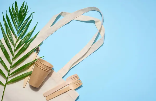 stock image White cotton bag, wooden forks and cups on a blue background. Waste recycling concept, zero waste