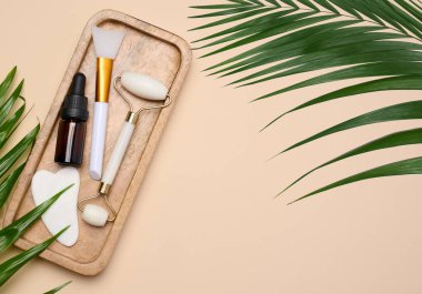 Kahverengi pipetli cam şişe, beyaz taş bir el masajı aleti ve bej arka planda kozmetik işlemler için bir kazıyıcı.