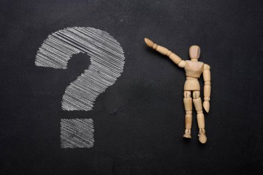 Tahta bir manken ve siyah tahtaya beyaz tebeşirle çizilmiş soru işareti. Belirsizlik ve merak kavramını betimliyor.