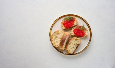 Kırmızı havyarlı sandviçler ve beyaz bir masada yuvarlak bir tabakta ekmek.