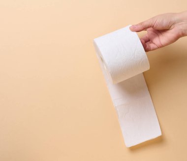 Bir kadın eli, bej arka planda beyaz bir tuvalet kağıdı tutuyor. 
