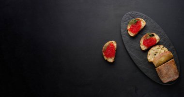 Siyah masadaki beyaz buğday ekmeğine kırmızı havyar, lüks ve gurme mutfağı kavramı. Boşluğu kopyala