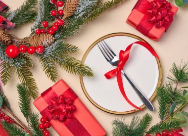 Çatallı boş yuvarlak beyaz tabak ve bej arka planda Noel dekoru olan paketlenmiş hediyeler, üst manzara. Neşeli arkaplan
