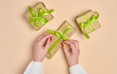 Bej arka planda yeşil kurdeleli hediye kutusunu tutan kadın eller. Yukarıdan görüntüle
