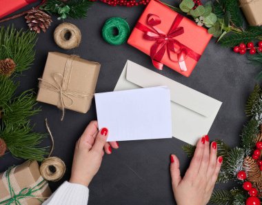Beyaz zarf ve siyah arka planda Noel çelengi, üst manzara. Kadın mektup yolluyor.