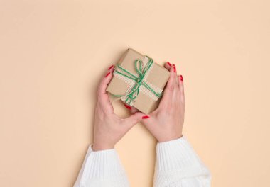 Bej arka planda hediye kutusunu tutan kadın eller. Yukarıdan görüntüle