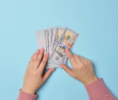 Kadın eli, yukarıdan bakıldığında mavi arka planda bir yığın kağıt para tutar.