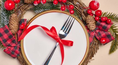 Çatallı boş yuvarlak beyaz tabak ve bej arka planda Noel dekoru olan paketlenmiş hediyeler, üst manzara. Neşeli arkaplan