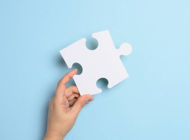 Bir kadın eli mavi arka planda beyaz bir yapboz parçası tutuyor. 