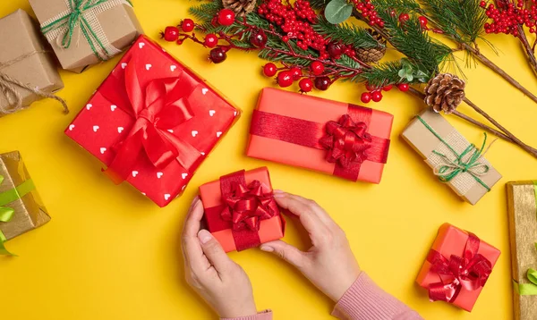 Woman is packing gifts, the pre-holiday bustle and preparations for Christmas. Gifts wrapped in red paper and tied with ribbon are laid out on the table