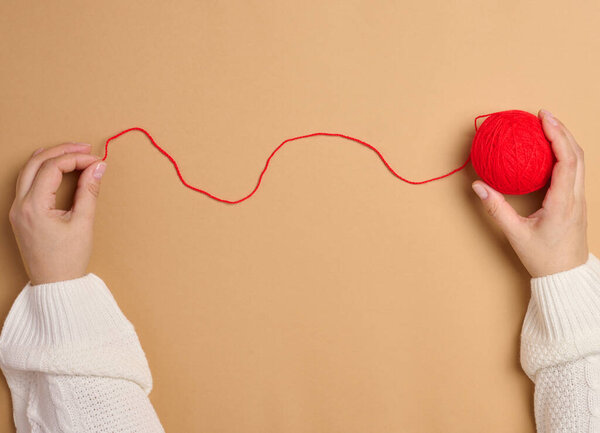 Two female hands holding a ball of red woolen threads for knitting, top view