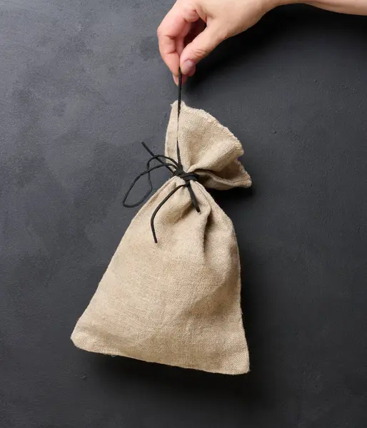 A woman\'s hand holds a canvas bag on a black background, the concept of a subsidy, help