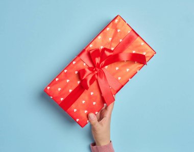 Kadın eli kırmızı kağıda sarılı bir kutuyu tutuyor ve kırmızı ipek bir kurdeleyle bağlanıyor.