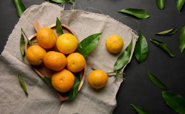 Siyah bir masanın üstünde yeşil yaprakları olan olgun bir mandalina.