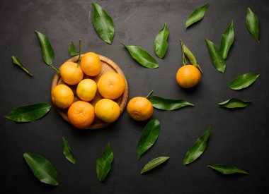 Siyah bir masanın üstünde yeşil yaprakları olan olgun bir mandalina.