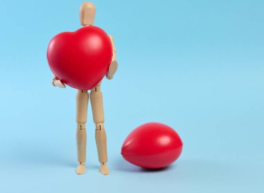 Mavi arka planda kırmızı bir kalp taşıyan tahta bir manken. Kan ve organ bağışı kavramını sembolize ediyor.