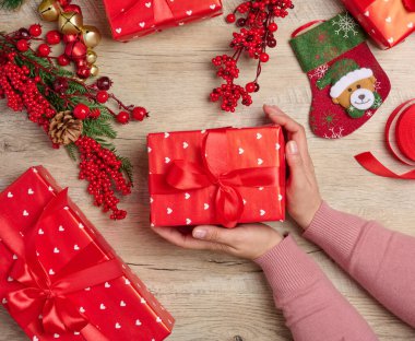 Kadın hediyeler paketliyor, bayram öncesi koşuşturması ve Noel hazırlıkları. Kırmızı kağıda sarılmış ve kurdeleyle bağlanmış hediyeler