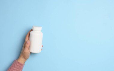 Mavi arka planda haplar için beyaz plastik bir şişe tutan iki kadın el. Boşluğu kopyala